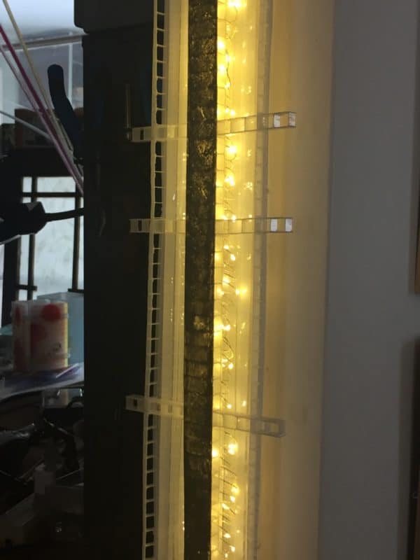 A one-inch wide strip of gold runs down the centre of a slender four-foot-long structure of polycarbonate struts and spars shot through with sparkling soft-white light.  Sculpture mounted on the wall-end of an archway.  Original LED light art.