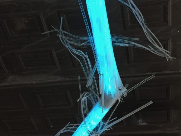 close-up of one joint of A Roar, A Boar, y Alice, a 22-foot-long sky-blue LED light sculpture by Lumencrafter, hung in the drive shed at Sourceworks Ceramics Studio for the 2018 Grey County Autumn Leaves Studio Tour. LED lights run through jointed acrylic tubes wrapped with strips of steel mesh and polycarbonate, glowing sky-blue against a dark stamped tin ceiling.. stunning; completely original.