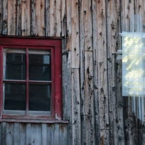 Solar Thing, unique solar-powered hand-made pale green four-foot long LED light sculpture by Lumencrafter mounted beside a red-framed window on the barn at Flesherton's Local Colour's 2020 Art Garden.