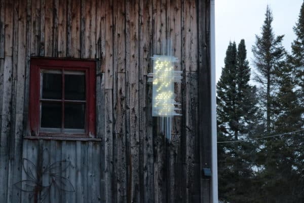 Solar Thing, unique solar-powered hand-made pale green four-foot long LED light sculpture by Lumencrafter mounted on the barn at Flesherton's Local Colour's 2020 Art Garden.