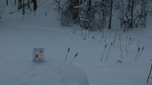 Light yet sturdy free-standing LED table light by Lumencrafter, light blue with deep pink splotches, glowing gently by a snow-covered pond with bullrushes.  6 inches high by four inch square base. Hand-painted plates of polycarbonate enclose dew drop LEDs wrapped around an inner polycarbonate core.  Indoor/outdoor. Suitable for evening al fresco dining or bedside mood lighting. Cordless; 3 AA batteries included.
