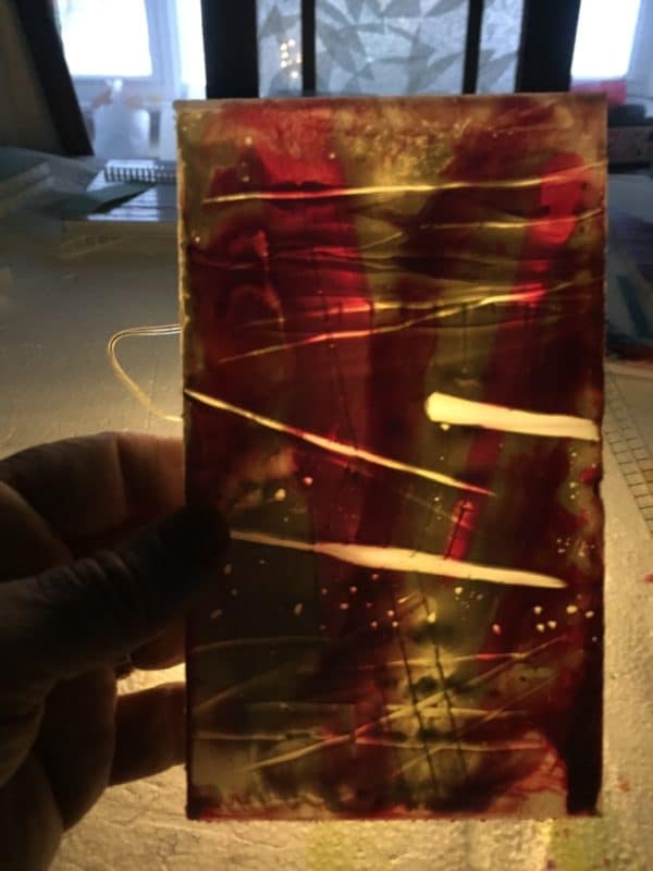 Light glows through pink and white encaustic panel of free-standing LED table light by Lumencrafter.  Light yet sturdy, 6 inches high by four inch square base. Hand-painted plates of polycarbonate enclose dew drop LEDs wrapped around an inner polycarbonate core.  Indoor/outdoor. Suitable for evening al fresco dining or bedside mood lighting. Cordless; 3 AA batteries included.