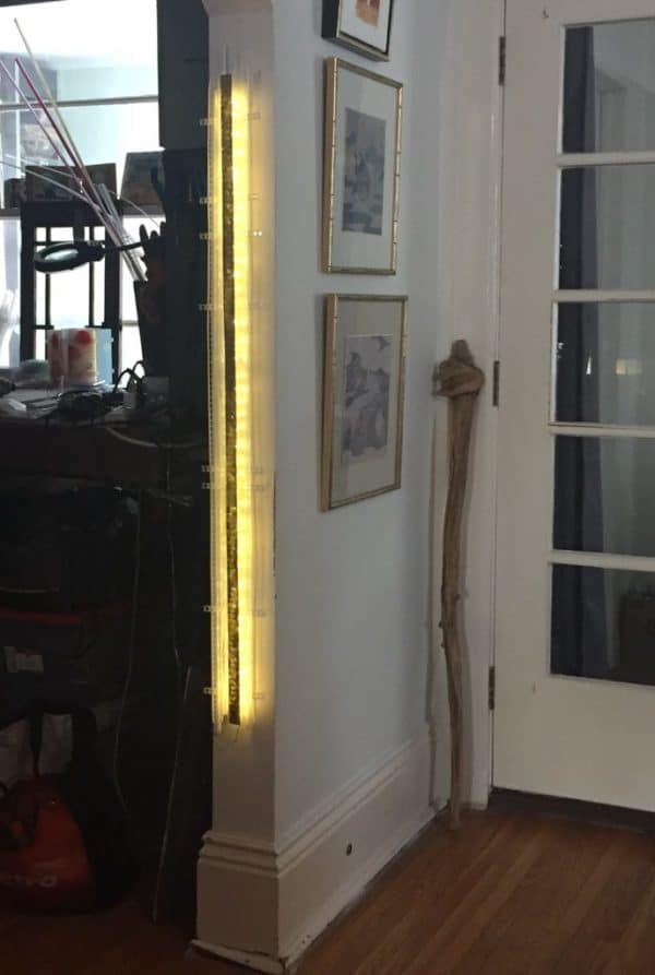 A one-inch wide strip of gold runs down the centre of a slender four-foot-long structure of polycarbonate struts and spars shot through with sparkling soft-white light.  Sculpture mounted on the wall-end of an archway.  Original LED light art.