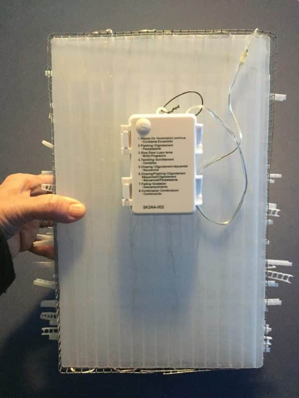 Reverse side of Box #1 showing battery options, rectangular white battery-powered LED light sculpture from Lumencrafter, soft white fairy lights shine behind a diffusion plate framed by a sturdy steel grid with several thin twinwall strips poking through, up and down, back and forth.