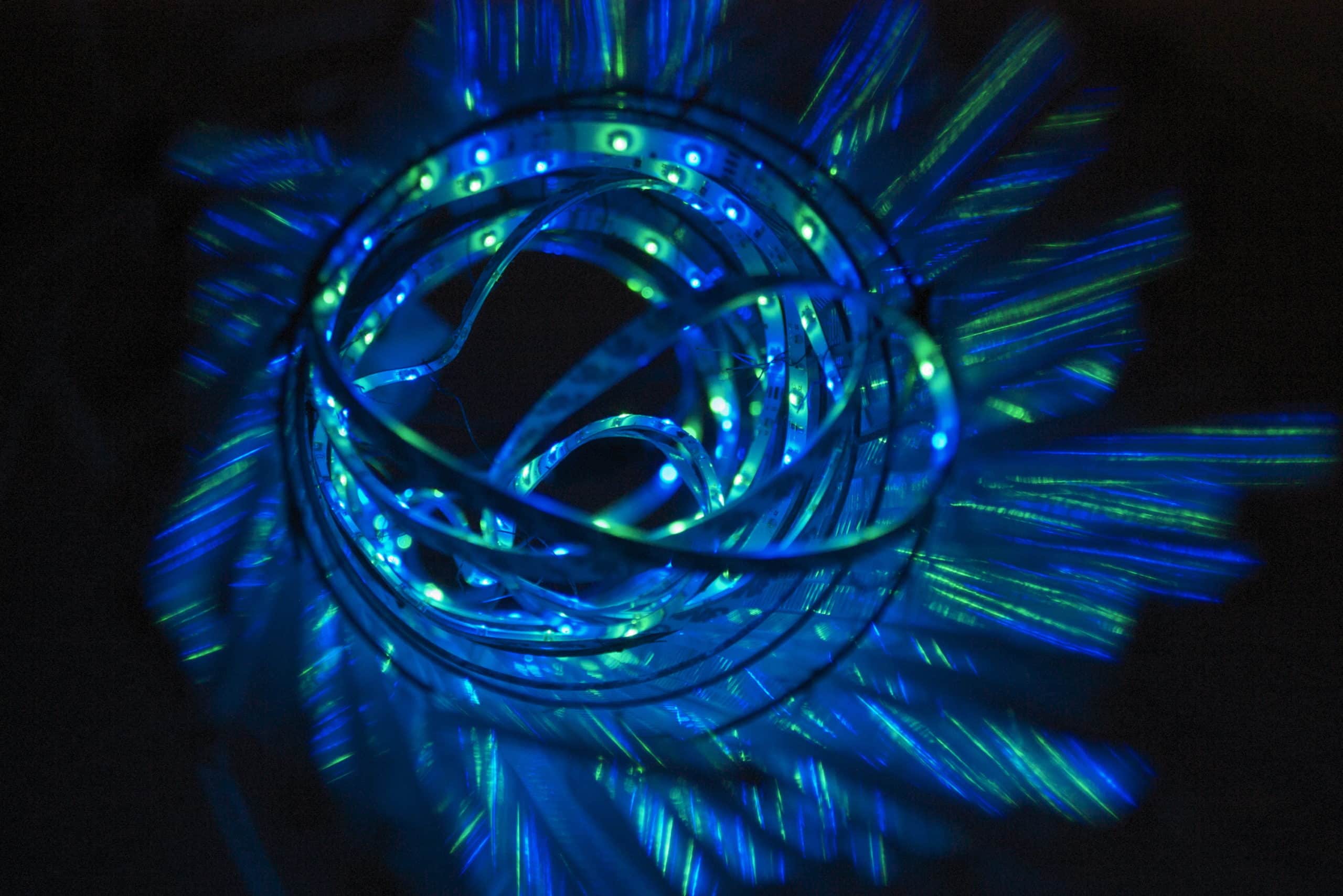 Blue pendant cylinder LED light sculpture seen from below, 4 feet long, pale blue lights shine through a veil of polycarbonate strips mounted on a wire frame, an explosion of form and colour.