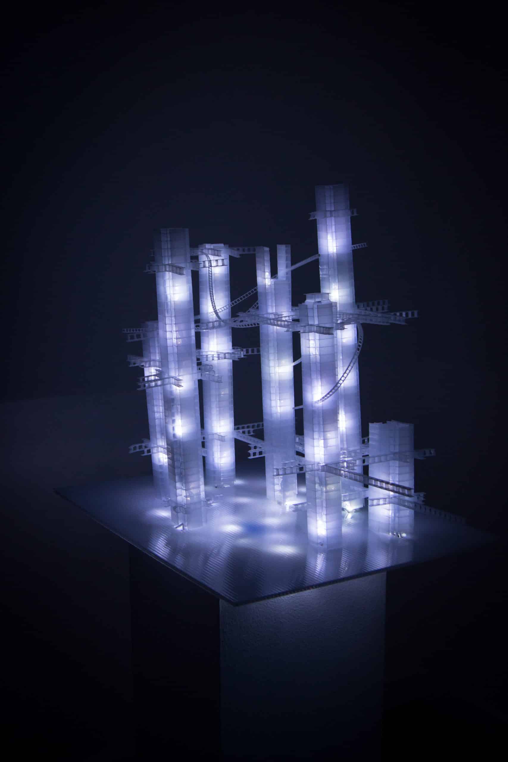 This Years' Model, a.k.a If You Lived Here, You'd be Home by Now, free-standing soft white original handmade Lumencrafter LED light sculpture, square columns of different heights connected by swirls of laddered polycarbonate twinwall strips, glowing blue-white at Arcadia Art Gallery, Toronto, 2014.