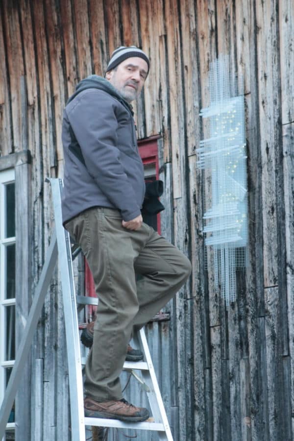 Solar Thing, unique solar-powered hand-made pale green four-foot long LED light sculpture by Lumencrafter being mounted by artist Reid Dennison on the barn at Flesherton's Local Colour's 2020 Art Garden.