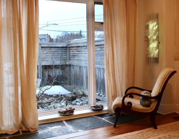 Solar Thing, unique solar-powered hand-made pale green four-foot long LED light sculpture by Lumencrafter, on living room wall facing picture window showing stone garden.