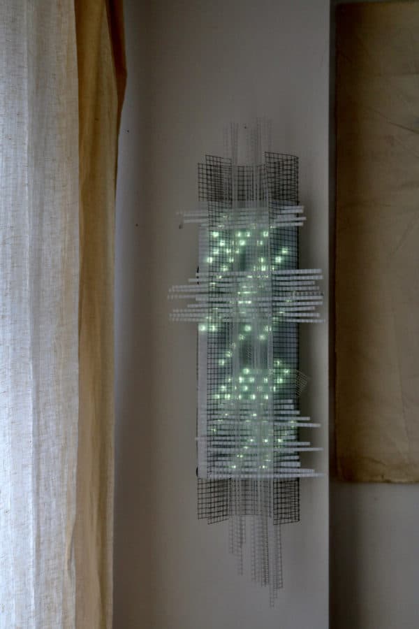 Solar Thing, unique solar-powered hand-made pale green four-foot long LED light sculpture by Lumencrafter, on living room wall in the soft light of dusk.