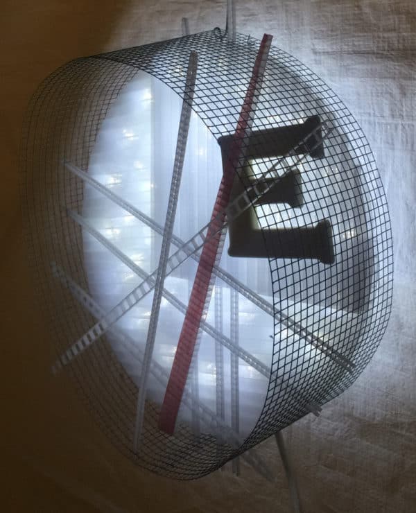 Runnin' On, original circular LED wall sconce light sculpture by Lumencrafter: A cool white LED rope light shines through a diffusion circle with large ceramic E and painted red pointer; polycarbonate strips poke through surrounding steel mesh cylinder. Sculpture shown at 2018 Grey County Autumn Leaves Studio Tour.