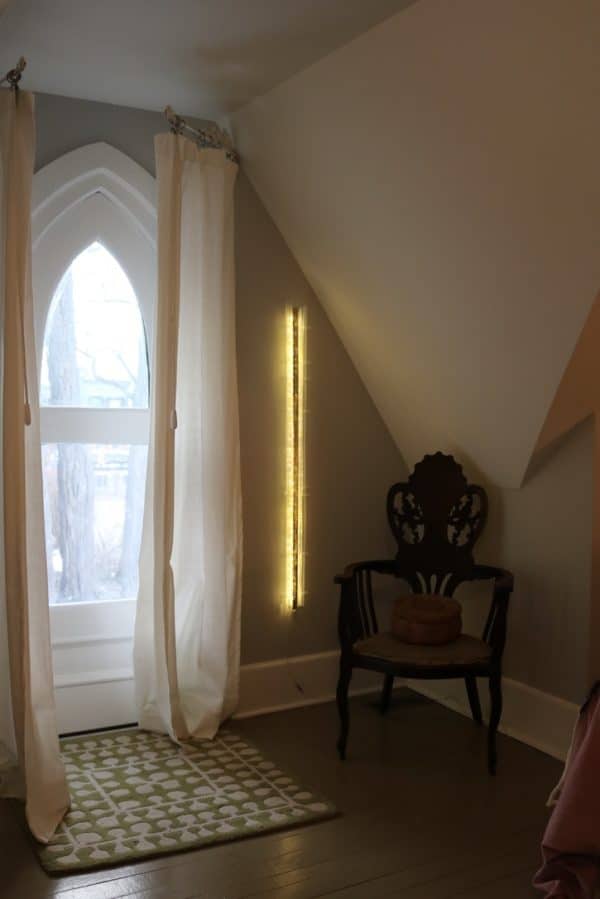 A one-inch wide strip of gold runs down the centre of a slender four-foot-long structure of polycarbonate struts and spars shot through with sparkling soft-white light.  Wall sculpture mounted in bedroom.    Original LED light art.