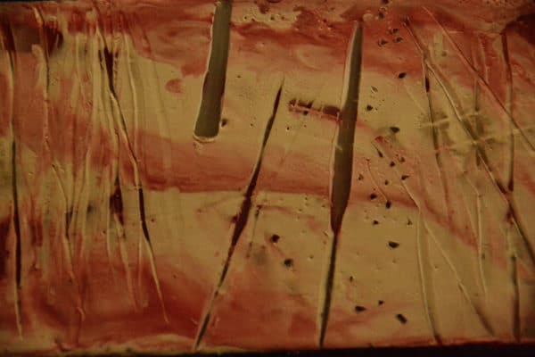 Close-up of pink and white encaustic panel of free-standing LED table light by Lumencrafter.  Light yet sturdy, 6 inches high by four inch square base. Hand-painted plates of polycarbonate enclose dew drop LEDs wrapped around an inner polycarbonate core.  Indoor/outdoor. Suitable for evening al fresco dining or bedside mood lighting. Cordless; 3 AA batteries included.