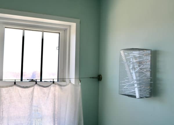 Box #1 original Lumencrafter wall sconce light sculpture mounted on bathroom wall by window.  Rectangular white battery-powered LED light sculpture, soft white fairy lights shine behind a diffusion plate framed by a sturdy steel grid with several thin twinwall strips poking through, up and down, back and forth.