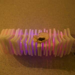 front view of Weight of Beauty, an LED wall-mounted light sculpture by Lumencrafter. A preserved blossom rests on layers of vertical polycarbonate glowing magenta-pink at the Grey Highlands Artists Collective 2017 exhibition, Sacred Spaces: Altars by Artists at The Gallery, L.E. Shore Library, Thornbury.